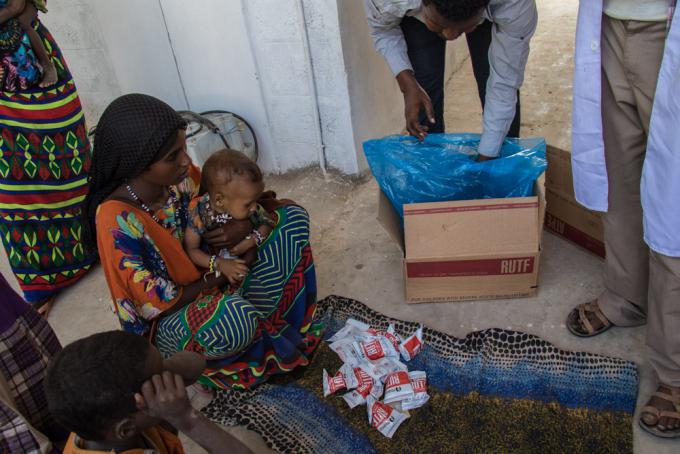 A mother receives a two-week supply of high nutrient peanut paste for her child who suffers from moderate acute malnutrition.